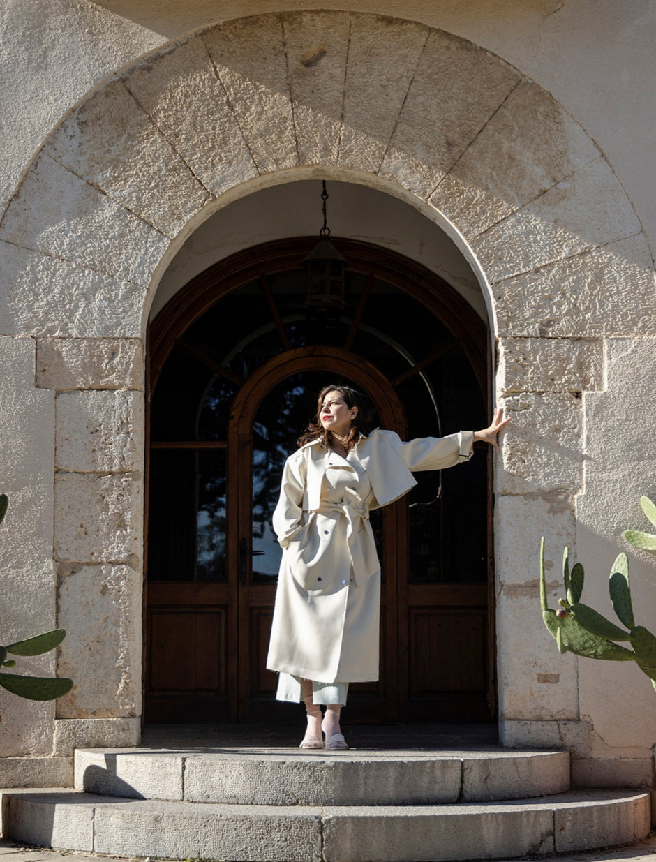 Ebru Gurlek in a white coat standing in an archway with potted plants on either side.